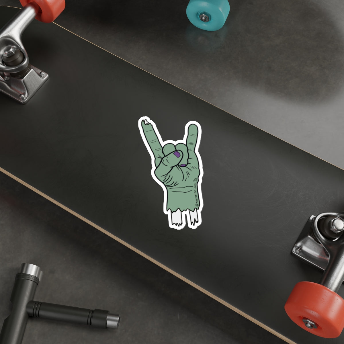 Skateboard with a green hand making a rock sign sticker on a black deck.