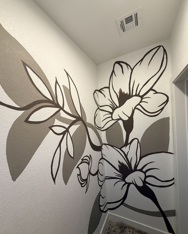 Black-and-white floral bathroom mural by Andy Carlson: large outlined lilies and a leafy branch with soft gray shadow shapes wrapping around a corner