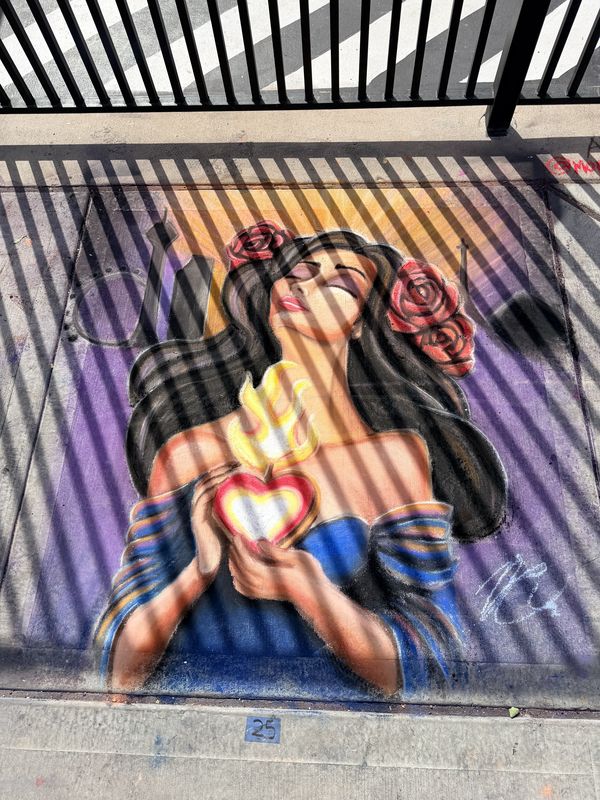 Sidewalk chalk mural by Andy Carlson: a woman with long dark hair and red roses, eyes closed, holding a glowing flaming heart against a purple and gold background